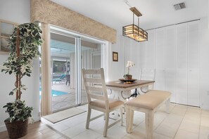 A dining area with a wooden table, two chairs, and a bench. There is a potted plant and a hanging light fixture.