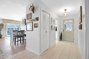 A spacious hallway with a dining area, white walls, and a large window.