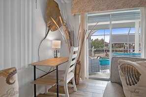 A modern room with a wooden table, a white chair, and a sofa with a pillow. There is a window with a view of a pool and a building outside.
