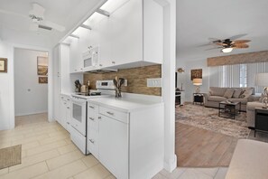 A modern kitchen with white cabinetry, a microwave, and a stove. There is a dining area with a sofa and a coffee table.