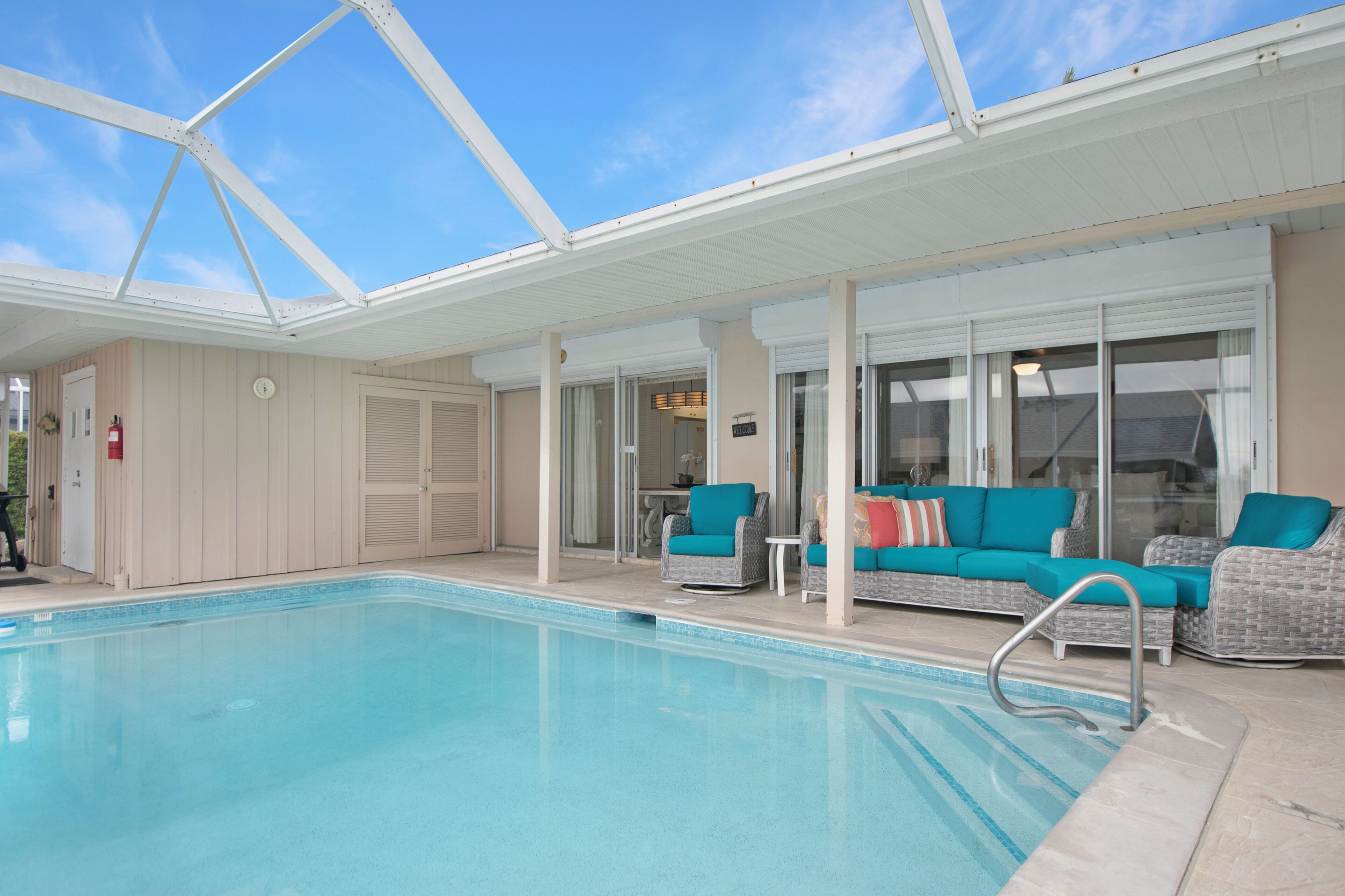 A covered swimming pool with lounge chairs and a glass door entrance.