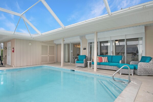 A covered swimming pool with lounge chairs and a glass door entrance.