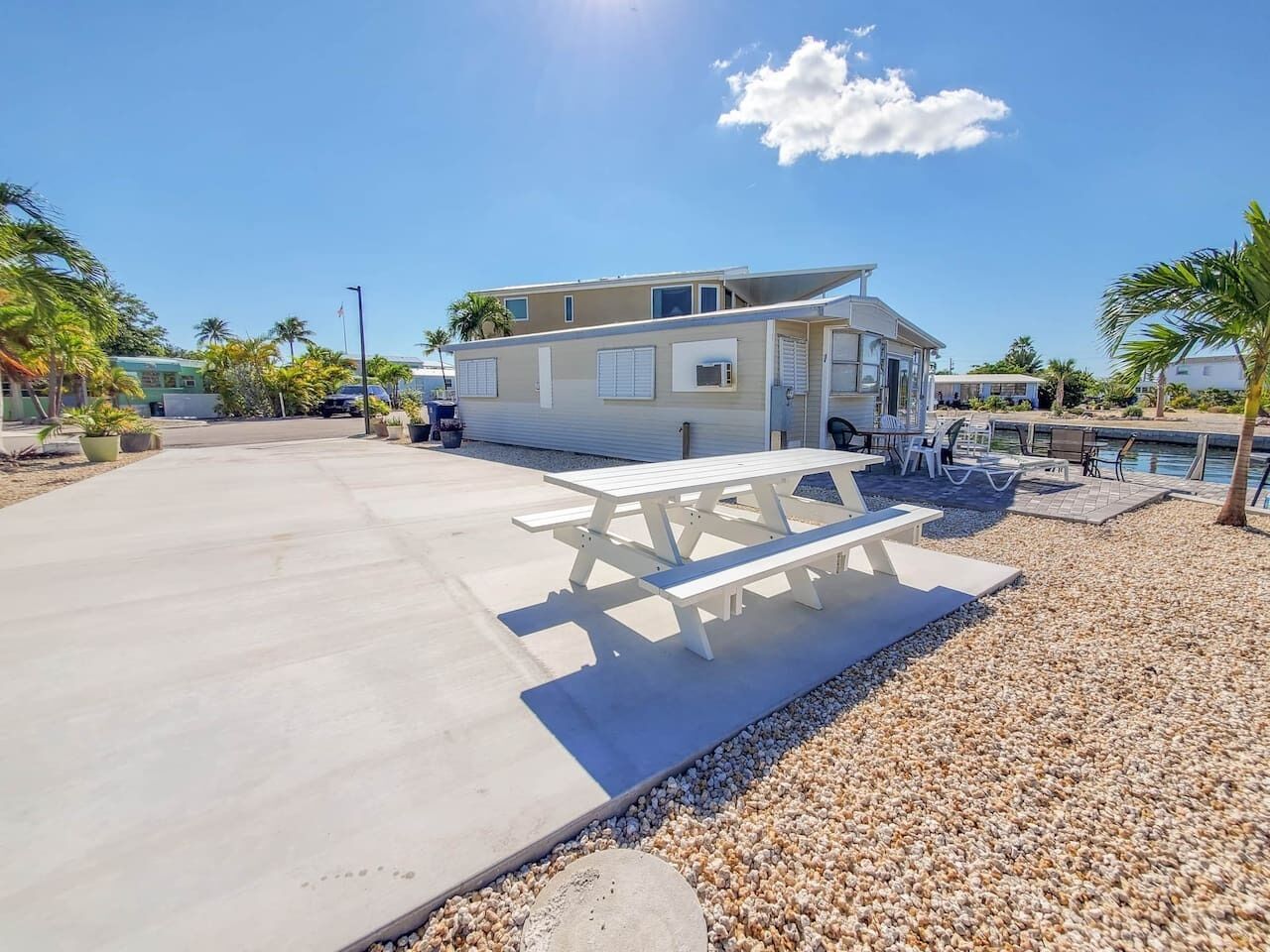 A beachfront property with a large concrete patio, a white picnic table, and a pool area.