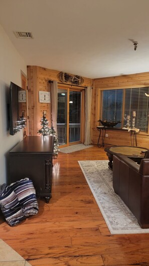 A cozy living room with a wooden floor, a dark wooden coffee table, a leather sofa, a small Christmas tree, and a fireplace.