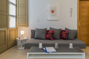 A modern living room with a grey sofa, two patterned pillows, a white coffee table with candles, a lamp, and a framed artwork on the wall.