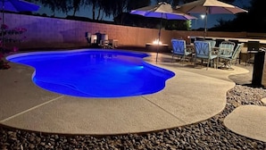 A swimming pool with a blue light, surrounded by patio furniture and umbrellas. - Glendale Pool Heated Pet Friendly (Glendale)