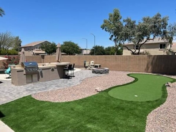 Un giardino sul retro con zona barbecue, una piccola piscina e un campo da golf in miniatura.