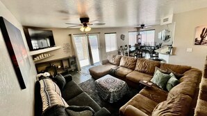 A living room with a sectional sofa, a coffee table, and a TV. There is a dining area with a table and chairs. - Glendale Pool Heated Pet Friendly (Glendale)