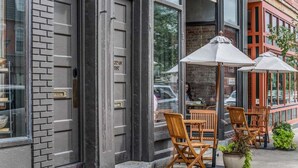 Un edificio con fachada de ladrillo, ventanas amplias y mesas al aire libre con sombrillas.