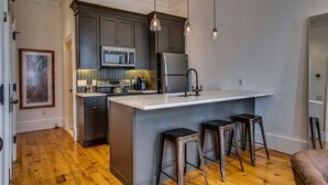 Una cocina moderna con armarios oscuros, una isla central con taburetes, un microondas y un refrigerador.
