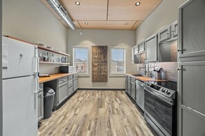 A modern kitchen with a wooden floor, stainless steel appliances, and a large window with blinds.