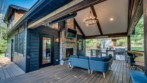 Eine überdachte Terrasse mit Kamin aus Stein, Sitzgelegenheiten im Freien und Grillplatz.