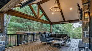 Ein überdachter Außenbereich mit Holzterrasse, Kamin aus Stein und einer Sitzecke mit Sofa und Sesseln.