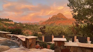 A stone patio with a hot tub and a waterfall feature, surrounded by a wooden fence and trees. - Panoramic Views, pool and 2 hot tubs, pool table (Sedona)