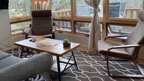 A cozy living room with a wooden table, two chairs, a sofa, and a TV. Large windows offer a view of the outdoors. - Panoramic Views, pool and 2 hot tubs, pool table (Sedona)