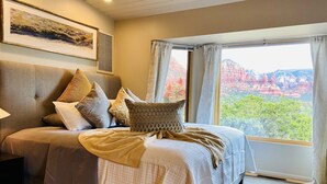A bedroom with a large bed, a headboard, a framed picture on the wall, and a window with a view of red rock formations. - Panoramic Views, pool and 2 hot tubs, pool table (Sedona)