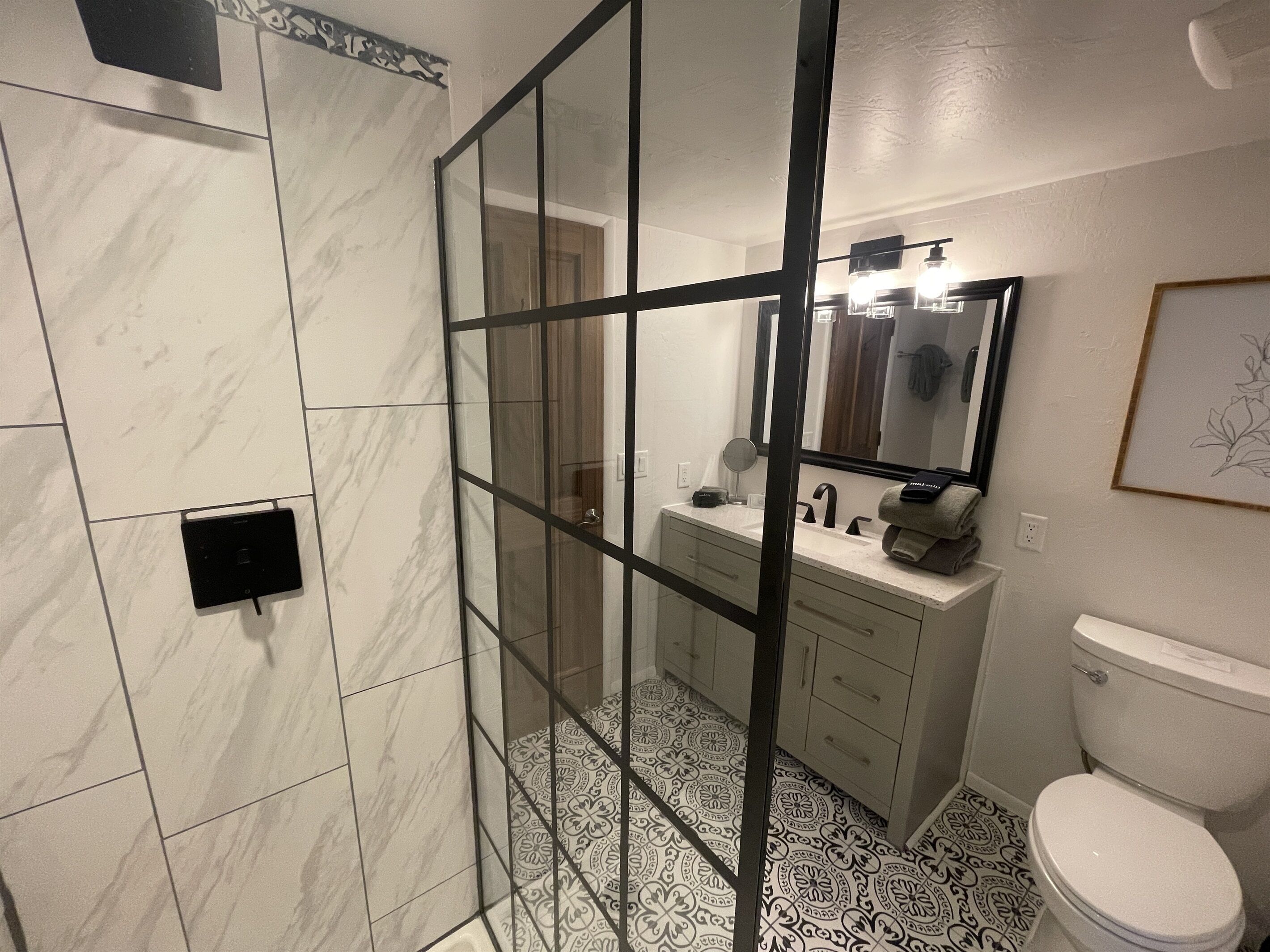 Une salle de bain avec une douche à parois de verre, des toilettes blanches et un meuble-lavabo avec un miroir.