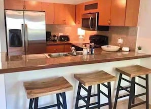 Une cuisine moderne équipée d’un réfrigérateur, d’un four à micro-ondes et d’un évier double en acier inoxydable. On y trouve également des tabourets en bois et un comptoir-bar.