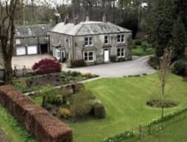 A large, two-story stone house with a well-maintained lawn and a hedge.