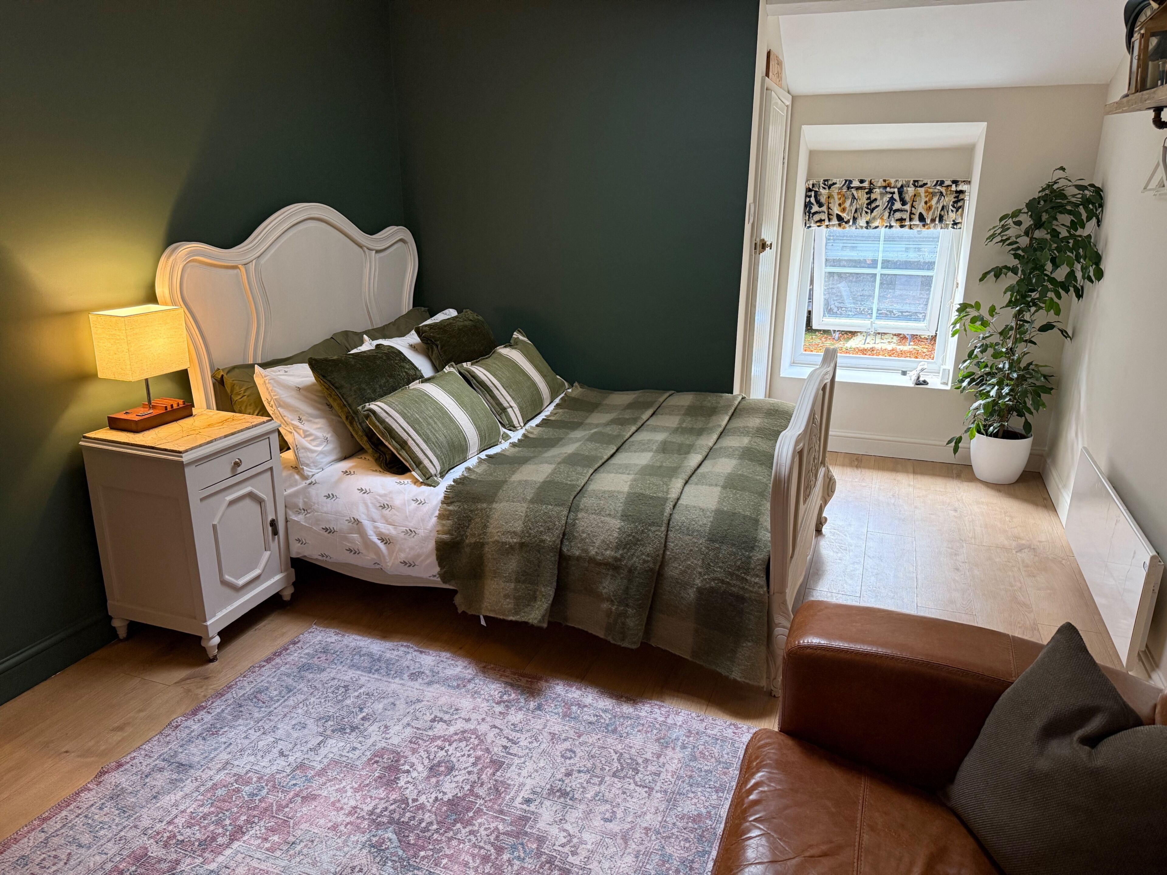 A bedroom with a bed, nightstand, lamp, and a view of the outdoors.