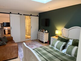 A bedroom with a bed, a dresser, a nightstand, a TV, and a sliding door leading to a shower area.