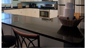 A kitchen with white cabinets, a microwave, an oven, and a refrigerator. There is a large island with a basket containing paper towels. - 8 BED 5 BATH Condo - Perfect for Multi-Family Vacations - Summer Week Deals (North Myrtle Beach)