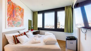 A hotel room with a bed, a large painting, a view of a cityscape, and a window with curtains. - Roof-top panorama suite with distant views over Vienna (Wien)