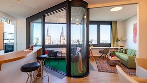 A modern living room with a large window, a green sofa, a wooden coffee table, and a bar area with stools. - Roof-top panorama suite with distant views over Vienna (Wien)