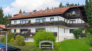Un hôtel à plusieurs étages, doté d’un toit en pente, de balcons ornés de plantes et d’une enseigne indiquant qu’il s’agit d’un centre de spa et de bien-être.