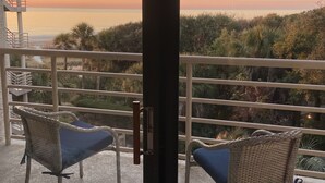 Ein Balkon mit Korbstühlen und Blick auf das Meer bei Sonnenuntergang.