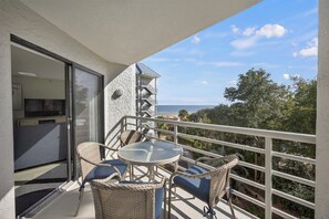 A balcony with wicker furniture, a glass door, and a view of the sea.