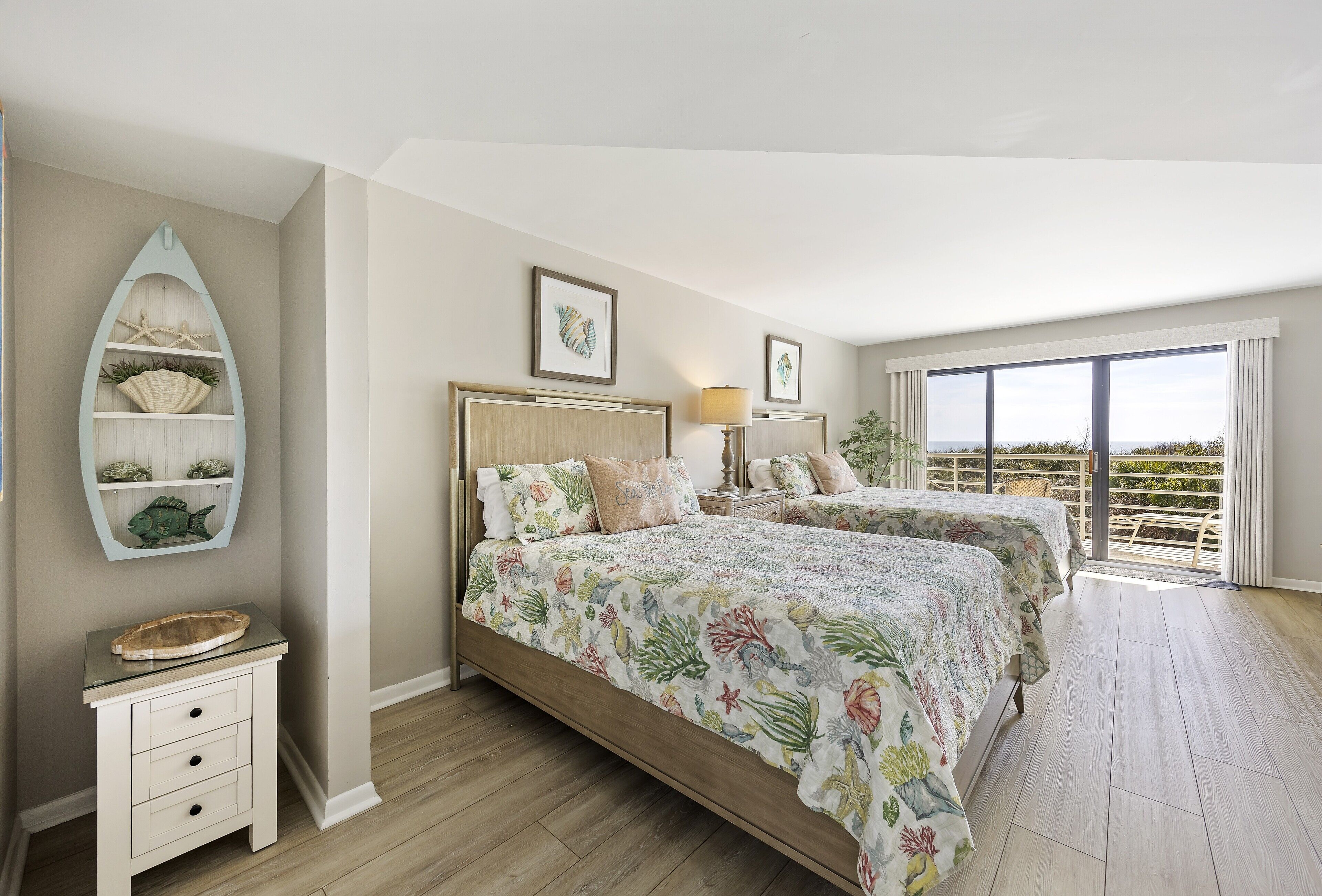 A bedroom with two beds, a nightstand, a decorative shelf with shells, and a view of the outdoors.