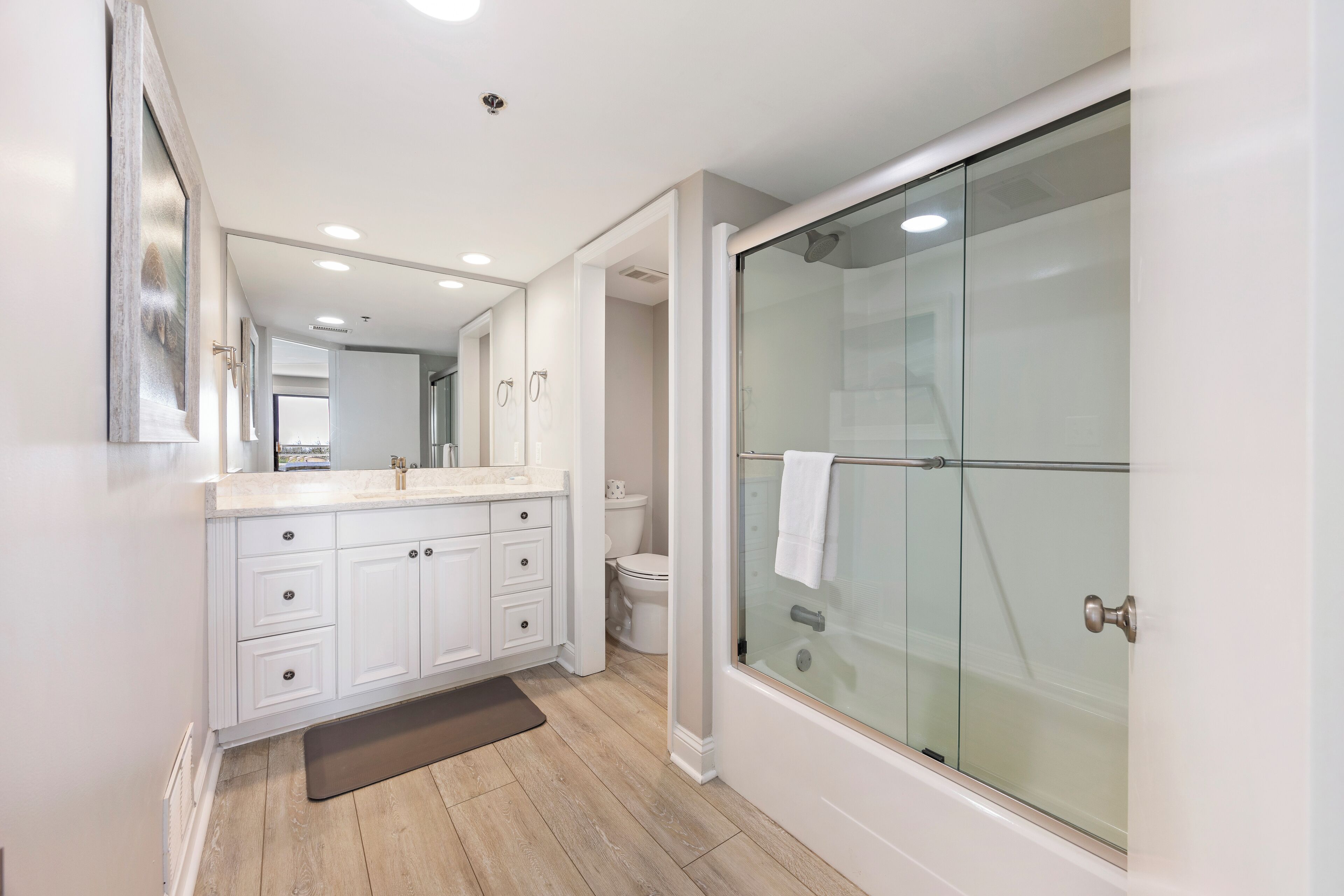 A modern bathroom with a glass-enclosed shower, white cabinetry, and a large mirror.