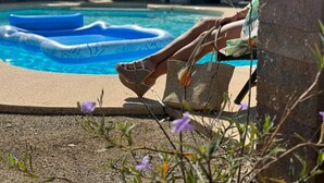 A person sitting by a pool with a floating ring, a wicker bag, and a small plant in the foreground. - The Valley View- Heated Pool/ Hiking/ Rooftop/ Gym/ WFH (Phoenix)