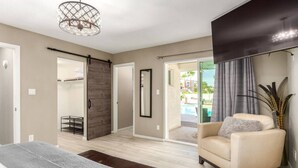 A modern bedroom with a large bed, a sliding door leading to a balcony, and a seating area with a chair and a small table. - The Valley View- Heated Pool/ Hiking/ Rooftop/ Gym/ WFH (Phoenix)