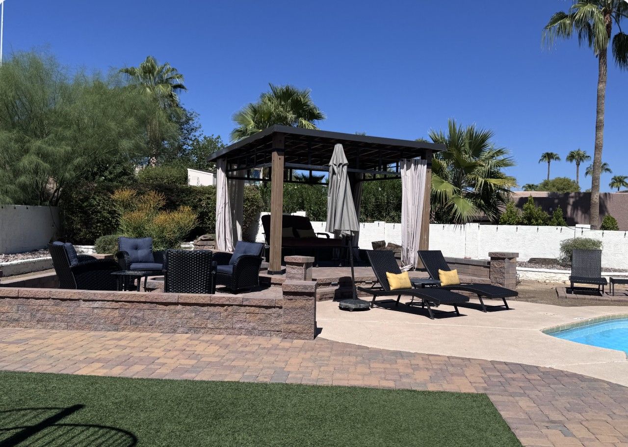 A covered outdoor seating area with lounge chairs and a barbecue grill.
