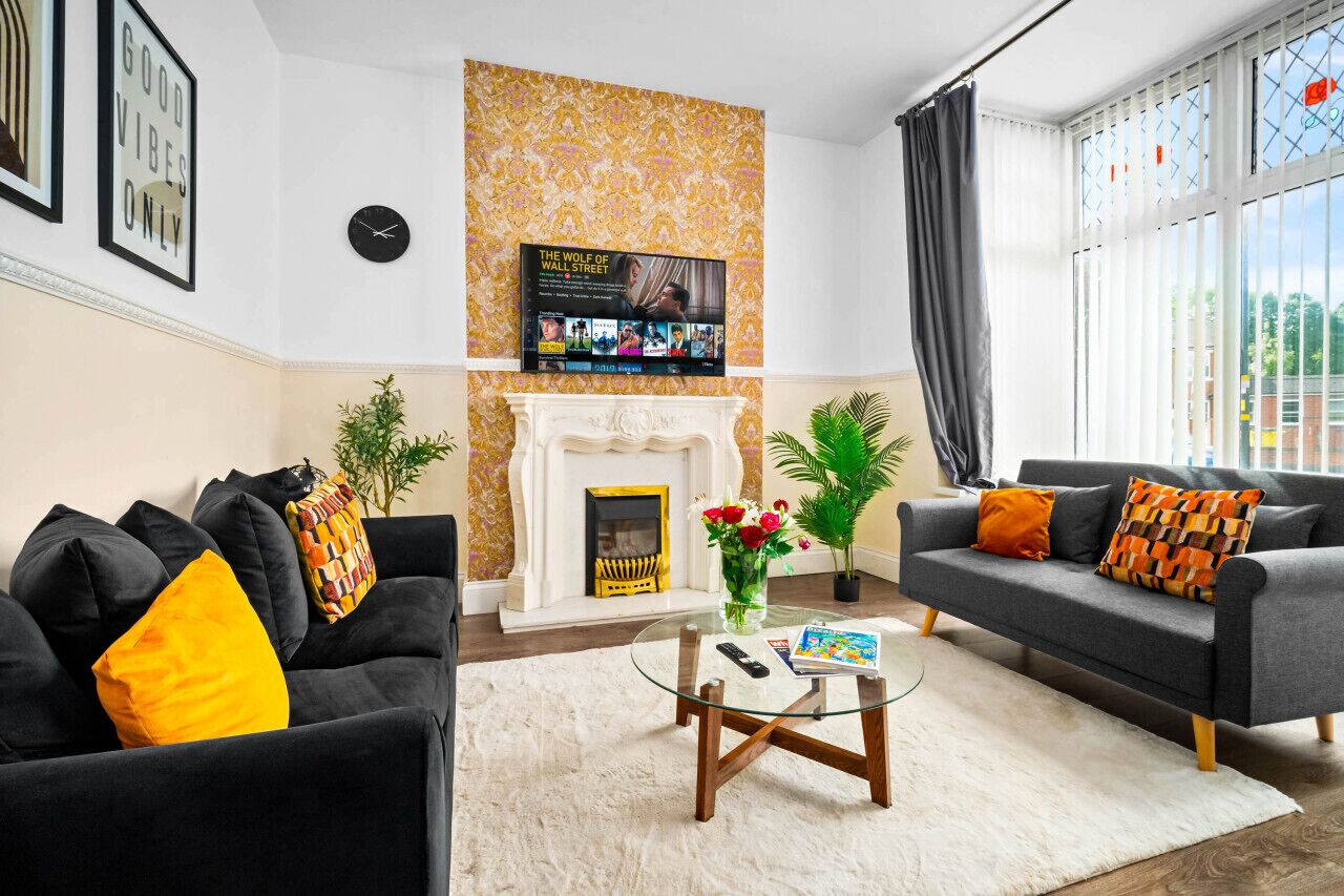 A living room with a fireplace, two sofas, a coffee table, and a TV mounted on the wall.