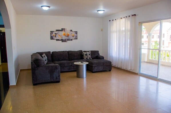 A living room with a sectional sofa, a round coffee table, and a large window with curtains.