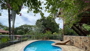 A swimming pool with a stone wall and a wooden deck. - WiFi+Pool+10min 2 Surf+Nature+Private+Quiet  (La Ermita)