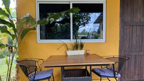 A yellow wall with a window, a wooden table, two wicker chairs, and potted plants. - WiFi+Pool+10min 2 Surf+Nature+Private+Quiet  (La Ermita)