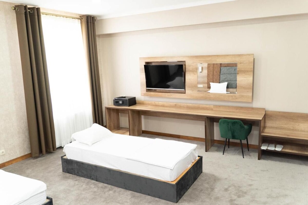 Quarto de hotel com cama, escrivaninha com computador, televisão e uma cadeira.