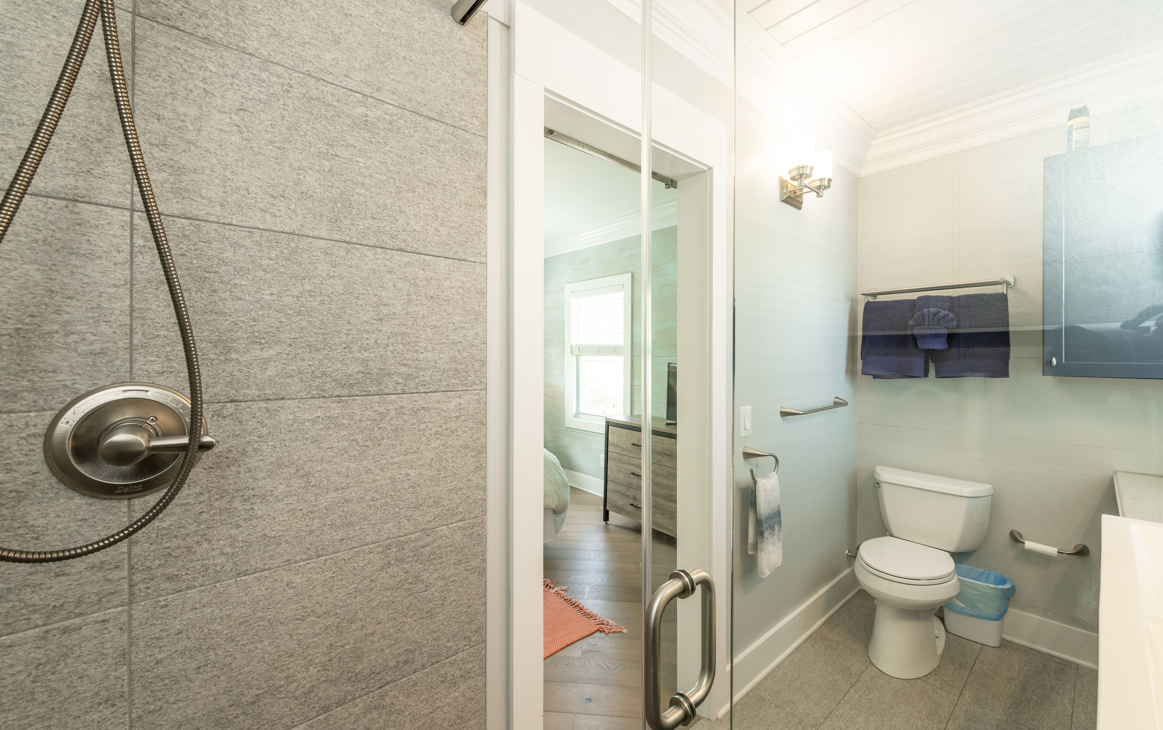 A bathroom with a shower, toilet, and a glass door leading to a bedroom.