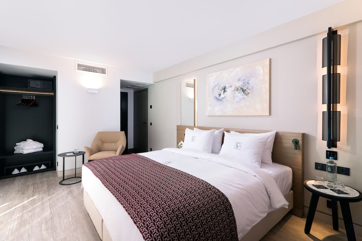 Moderni hotellihuone, jossa on suuri sänky, oleskelualue, vaatekaappi ja seinään kiinnitetty valaisin.