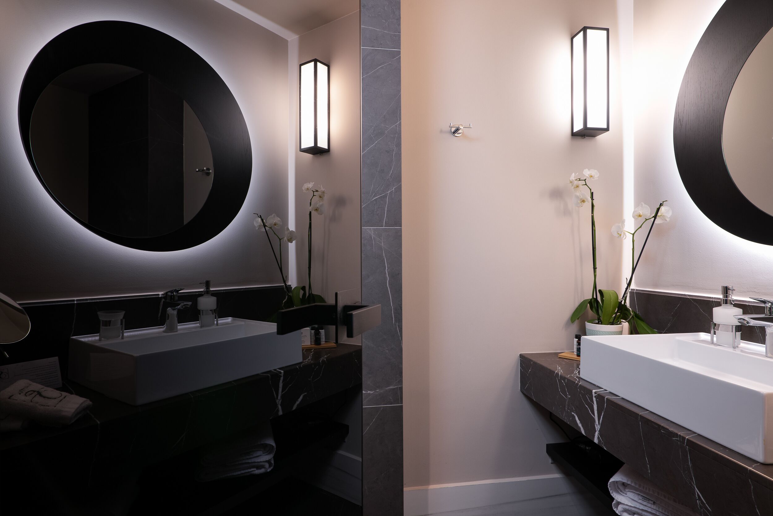 Een moderne badkamer met twee wasbakken, een grote spiegel en wandlampen.