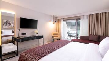 A hotel room with a large bed, a desk with a flat-screen TV, a chair, and a balcony with curtains.