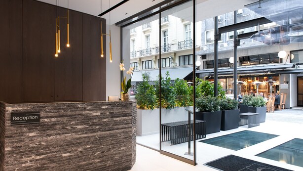 A reception area with a marble reception desk, potted plants, and a glass entrance leading to a courtyard with outdoor seating and a view of the building's exterior. - S Hotel Boutique Thessaloniki (Thessaloniki)