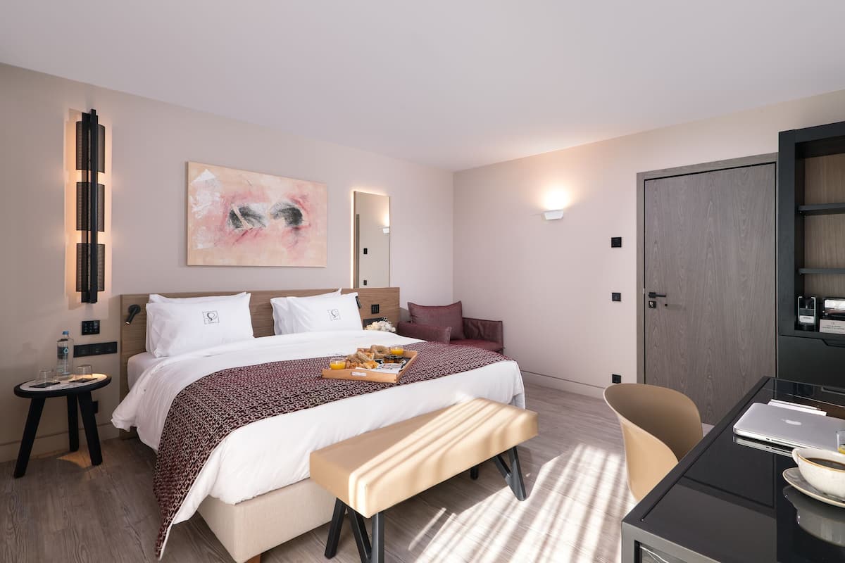 Moderni hotellihuone, jossa on suuri sänky, yöpöytä, jossa on aamiaistarjotin, työpöytä kannettavalla tietokoneella sekä suuri peili.