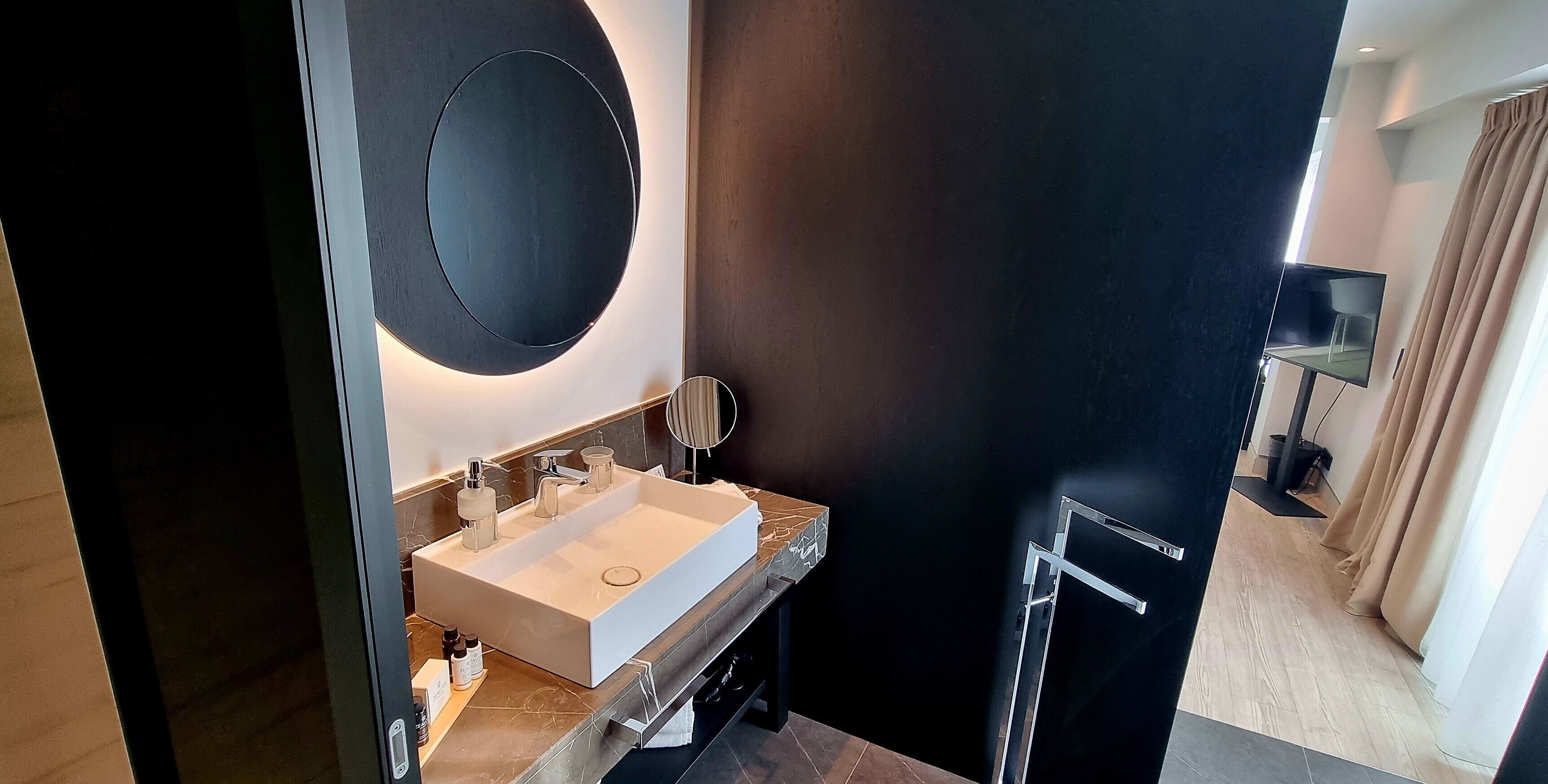 Une salle de bain moderne avec un grand miroir, un lavabo rectangulaire et un mur de couleur sombre.