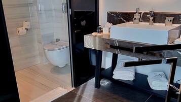 A modern bathroom with a glass shower enclosure, a large round mirror, and a vanity with a marble countertop.