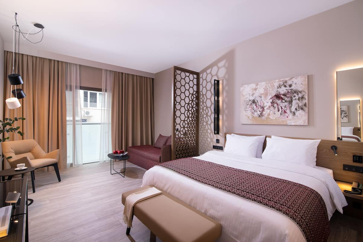 Hotellihuone, jossa on suuri sänky, työpöytä, tuoli, pieni pöytä ja penkki.